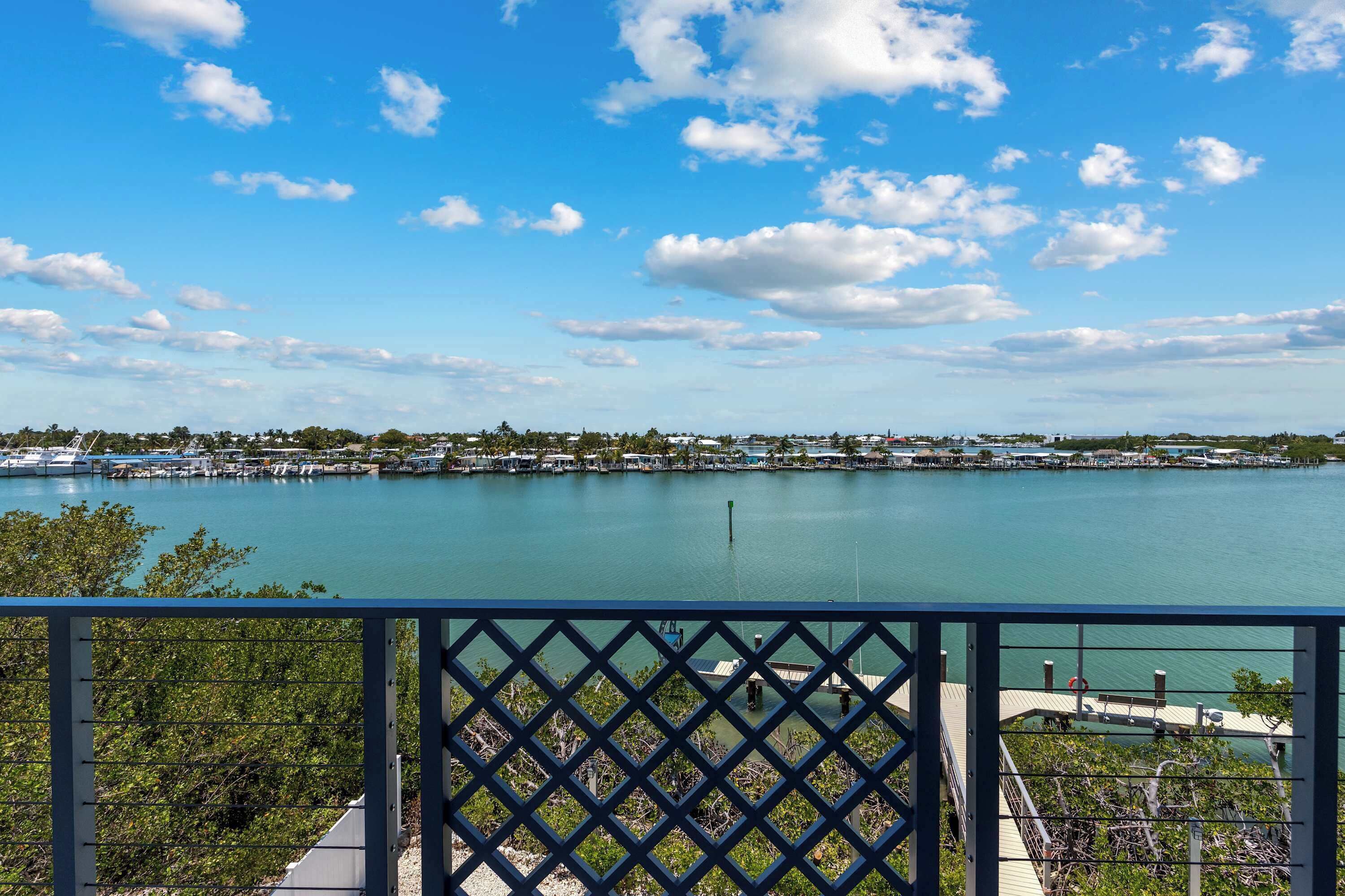 A waterfront view from a balcony with a lattice railing, a dock, and a calm lake.