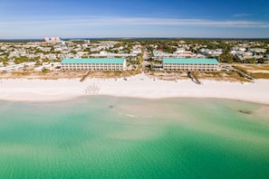 An aerial view of a coastal hotel with two large buildings, a sandy beach, and clear turquoise waters. - Crystal Sands110A • Luxe Remodel, Steps to the Sand (Destin)