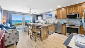A modern kitchen with wooden cabinets, stainless steel appliances, and a view of the ocean through large sliding glass doors. - Crystal Sands110A • Luxe Remodel, Steps to the Sand (Destin)