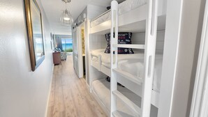 A narrow hallway with white bunk beds, a wooden floor, and a view of the sea through an open door. - Crystal Sands110A • Luxe Remodel, Steps to the Sand (Destin)
