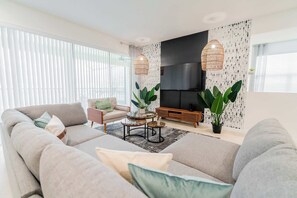 Een moderne woonkamer met een bank, fauteuil, salontafel en grote ramen.