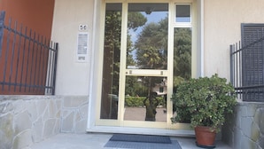 Une entrée d’immeuble avec une porte en verre, une plaque portant le numéro « 56 », une plante en pot et un portail en métal.
