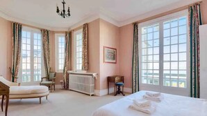 Un dormitorio con una cama grande, una silla, un radiador y una ventana con cortinas.