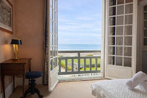 A room with a bed, a desk with a lamp, and a view of the ocean through an open door.