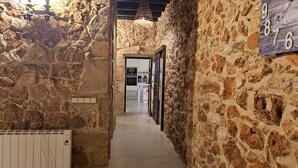 Corredor com paredes de pedra, um radiador, um relógio e um vislumbre de uma cozinha.