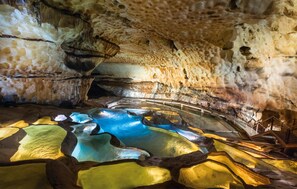Interno di una grotta con formazioni rocciose naturali e una vasca d'acqua specchiante.