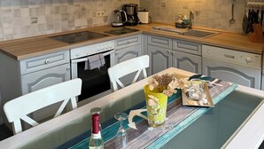 Eine Küche mit weißen Schränken, einer Holzauskładung, einer Pendelleuchte und einem Tisch, gedeckt mit einer Vase, Kerzen und einer Flasche.