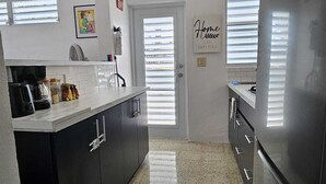 A modern kitchen with a refrigerator, dark cabinets, a countertop, and a door with a window.