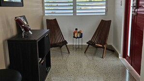 A compact room with two wooden chairs, a small table with items, a black cabinet, and a door with a red frame.