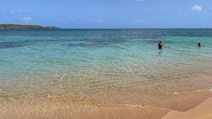 A beach with clear turquoise water, a sandy shore, and a distant island.