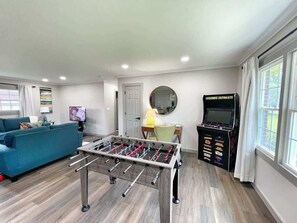 A living room with a foosball table, a sofa, a television, and a foosball cabinet.