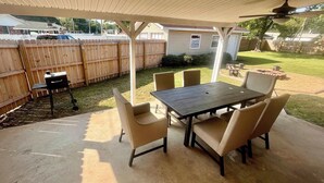Un patio cubierto con una mesa, sillas, una parrilla y una valla de madera al fondo.