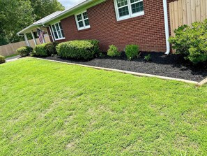 A residential house with a well-maintained lawn, a wooden fence, and a variety of shrubs. - Corporate Stay: 3BR, Arcade, Patio & Fast WiFi (Decatur)