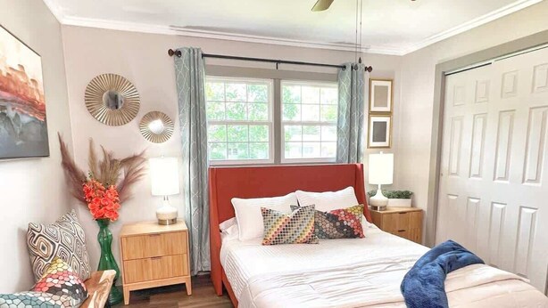 Un dormitorio con cama, mesita de noche, silla, ventana y puerta.
