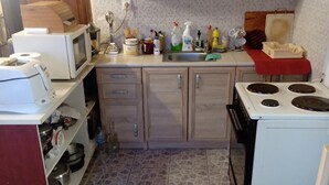 Una cocina compacta con electrodomésticos básicos, armarios de madera y suelo de baldosas.