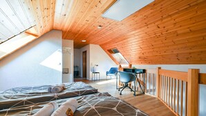 Een gezellig slaapkamer op zolder met houten balken, een schuine plafond en dakraam. Er staan twee bedden met opgerolde handdoeken, een bureau en een stoel.