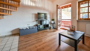 Een moderne woonkamer met houten vloer, een televisie op een zwart meubel, een klein tafeltje met een fles en een trap.