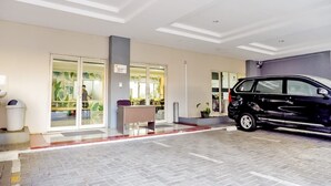 Entrada de un edificio con un coche estacionado, un contenedor de basura y un banco.