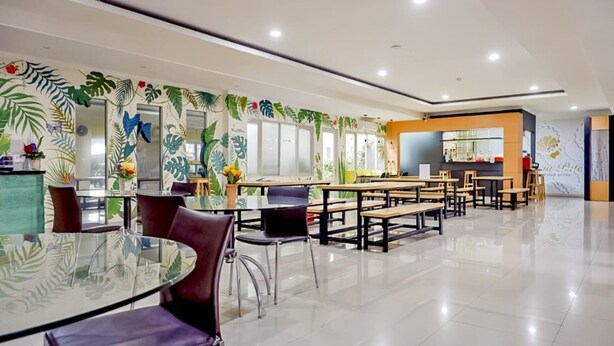 Un comedor moderno con una mesa de vidrio y sillas moradas, rodeado de bancos de madera y una pared decorada con motivos de hojas tropicales.