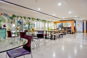 A modern dining area with a glass table and purple chairs, surrounded by wooden benches and a wall decorated with tropical leaf patterns. - OYO Life 93383 Wisma Kencana Puteri (Jakarta)