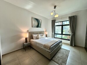 Ein modernes Schlafzimmer mit einem großen Bett, zwei Nachttischlampen, einer Deckenleuchte, einem Fenster mit Vorhängen und einem Gemälde an der Wand.