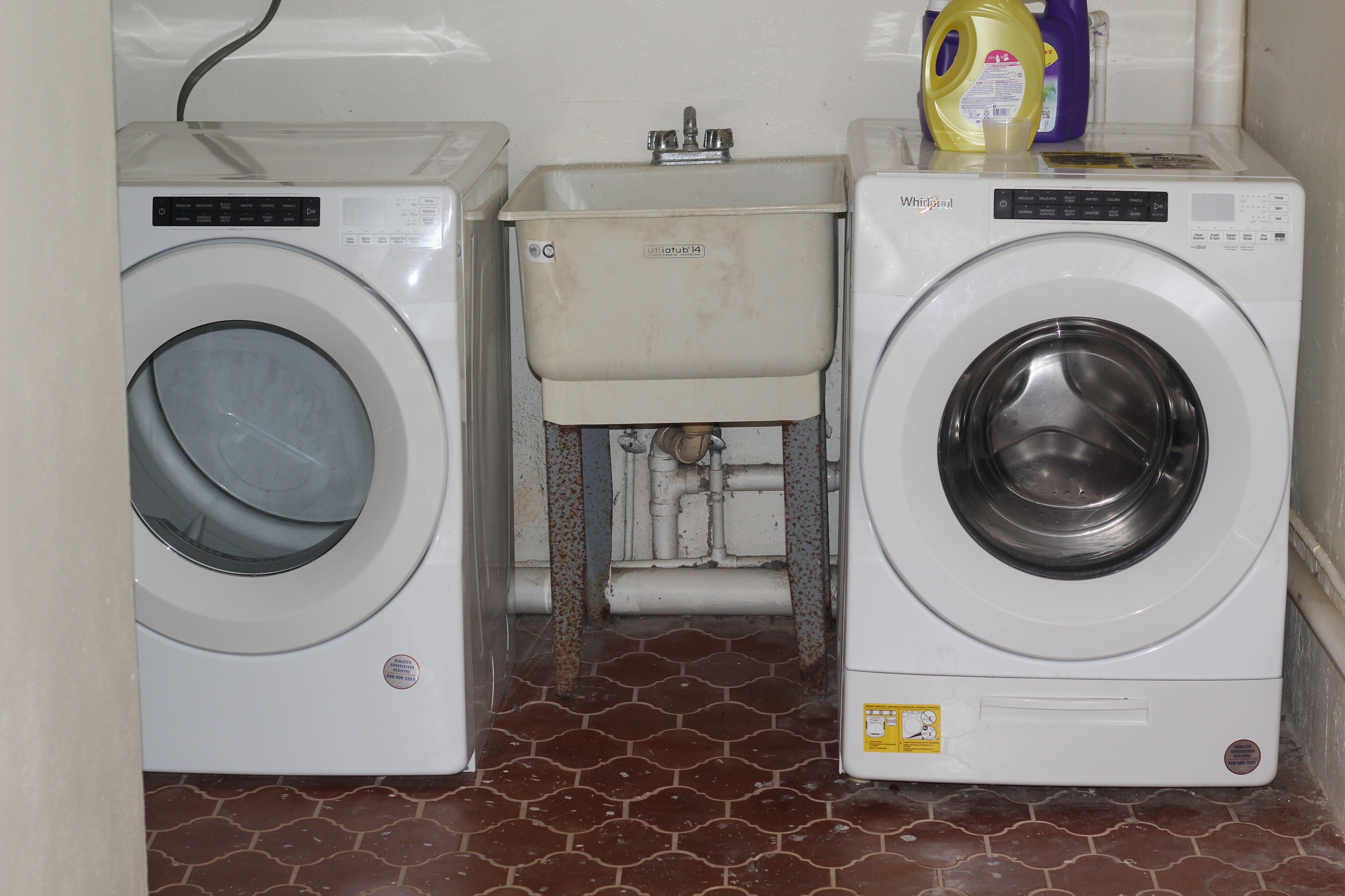 Two front-loading washing machines next to a small sink with a hose.