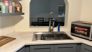 Een keuken met een RVS spoelbak, een houten snijplank en een magnetron.