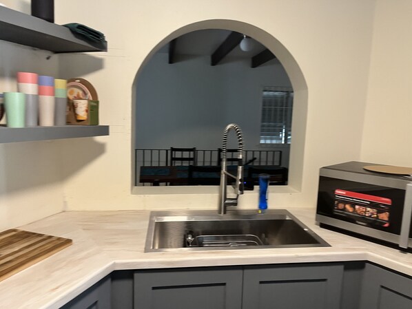 A kitchen with a stainless steel sink, a wooden cutting board, and a microwave.