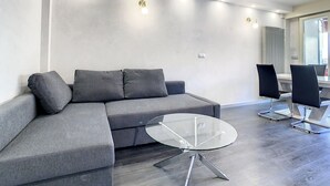 A modern living room with a grey sectional sofa, a glass coffee table, and black chairs.