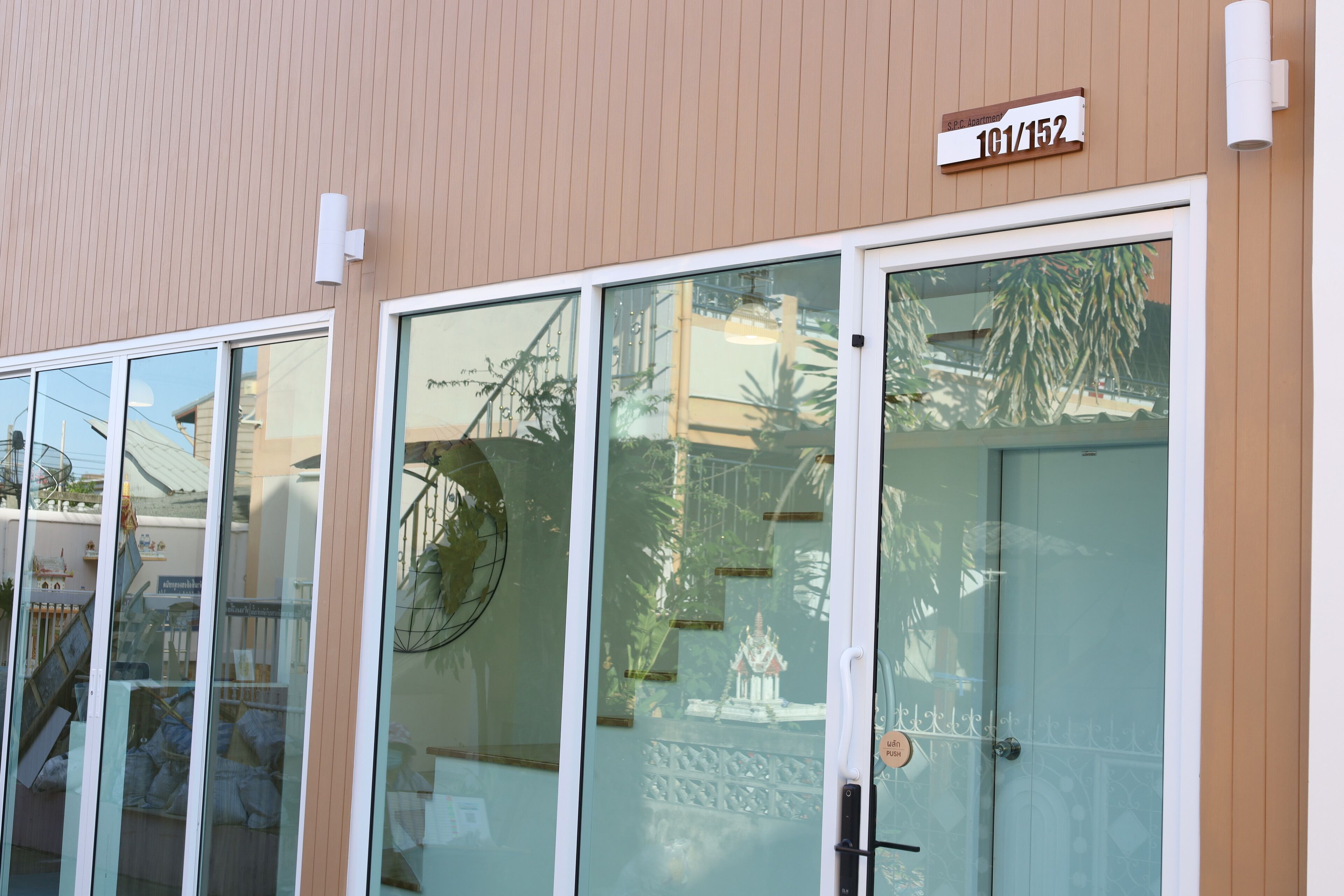 A building facade with large glass doors, a sign indicating room numbers 101/152, and a reflection of palm trees and a statue.