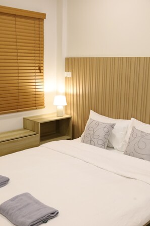 Una habitación de hotel con una cama, una mesita de noche con lámpara y una ventana con persianas.