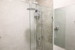 Un baño moderno con ducha envuelta en vidrio, azulejos de mármol y puerta de cristal.