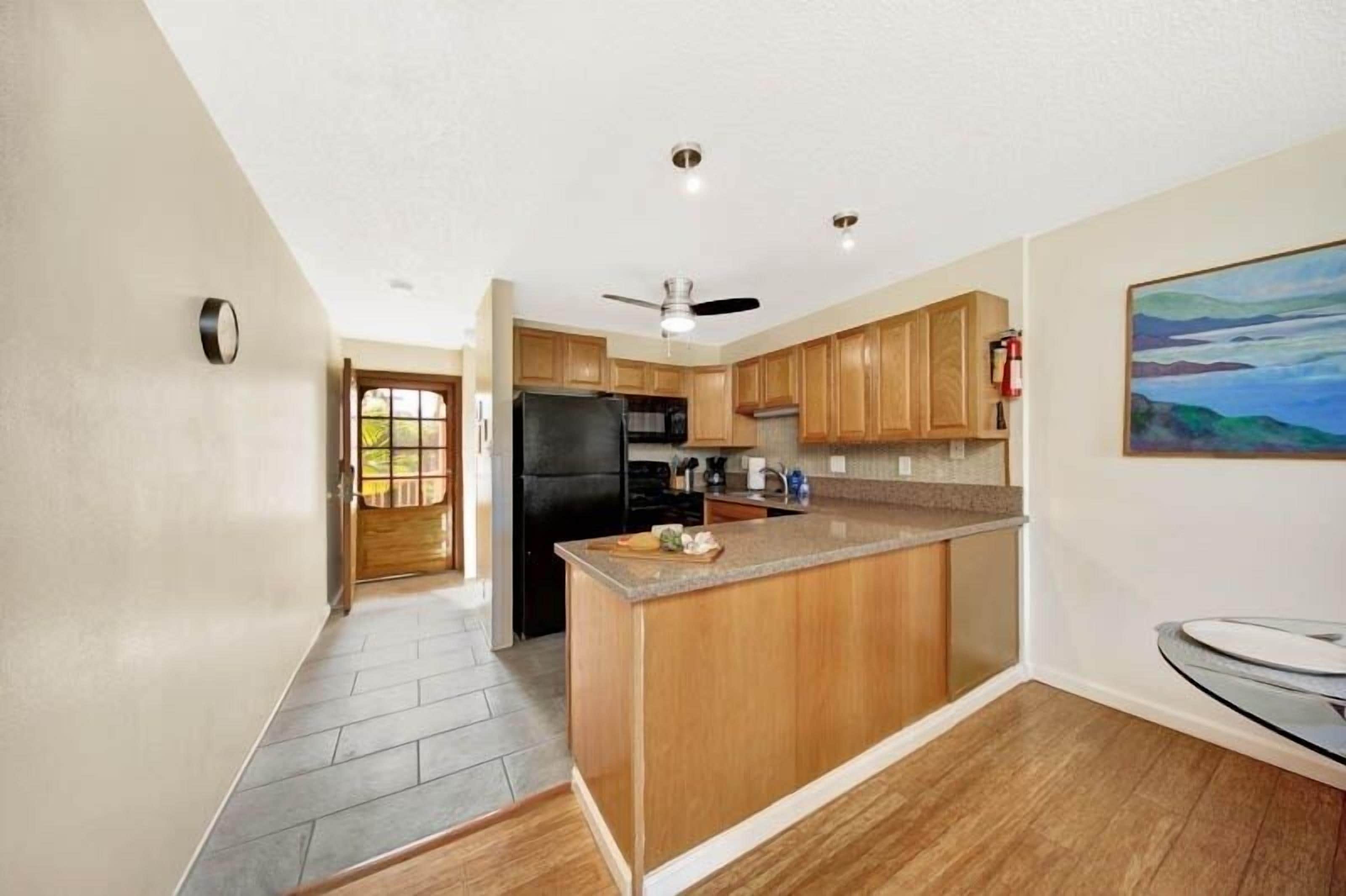 A kitchen with wooden cabinets, a black refrigerator, a granite countertop, and a ceiling fan.
