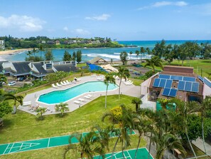 A resort with a swimming pool, sun loungers, a tennis court, and a view of the ocean. - Kauai Banyan Harbor B24 2 Bedroom Condo (Lihue)