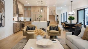 A modern kitchen with wooden cabinets, a central island, and pendant lighting. - Designer Digs 9 Bedroom Home (St. George)