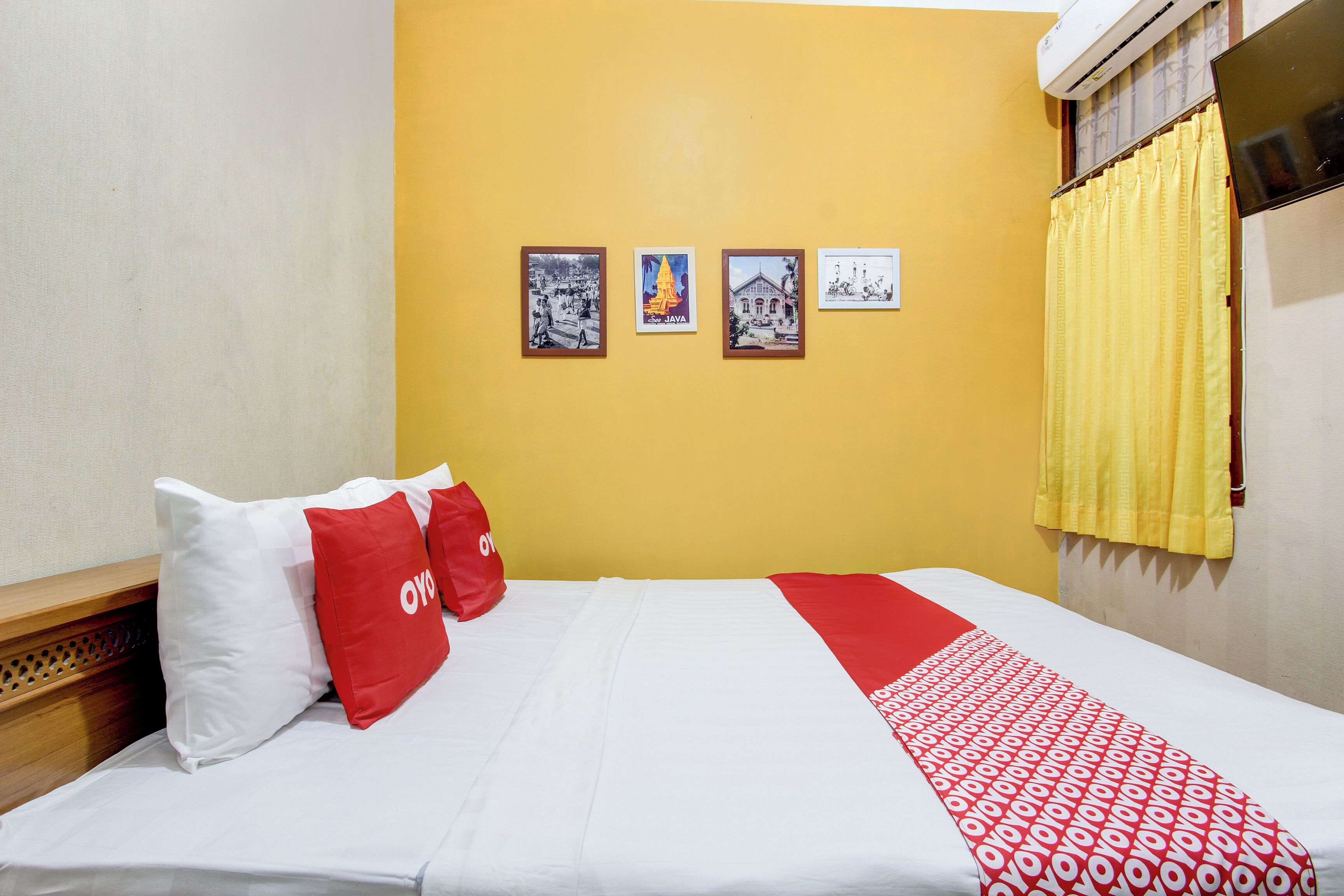 A hotel room with a bed, a yellow wall, and four framed pictures.