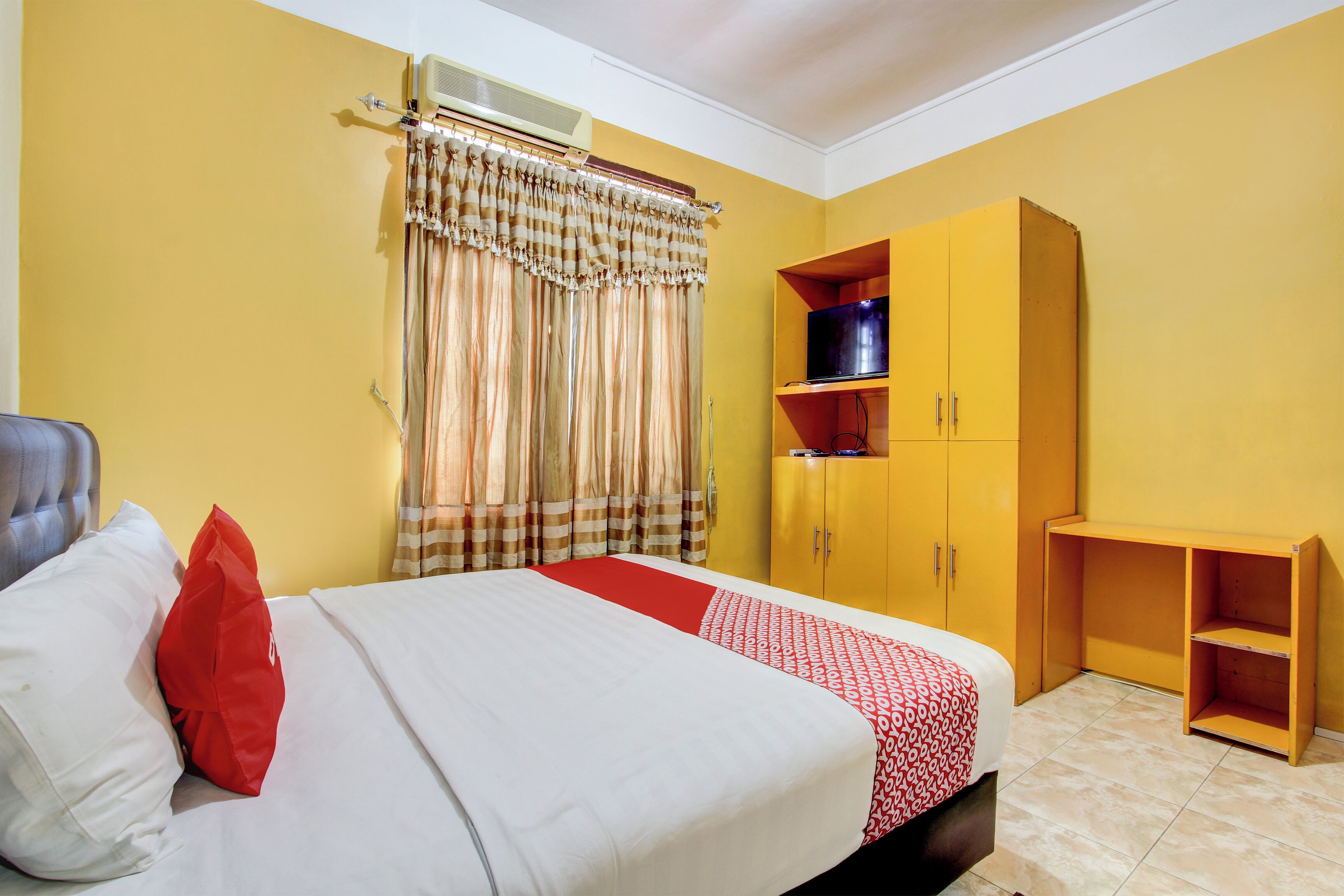 Un dormitorio con cama, armario, televisor y ventana con cortinas.