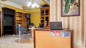 A reception desk with a laptop, a refrigerator, and a coffee machine. There are wooden cabinets and a painting on the wall. - Hotel O Griya Pius Syariah Malioboro (Yogyakarta)