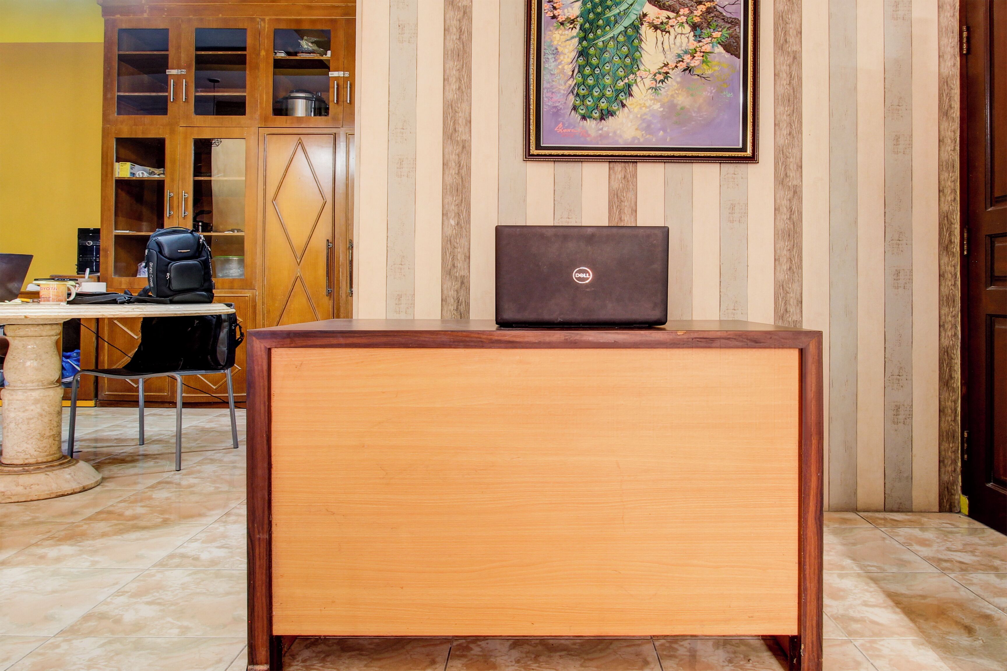 A wooden desk with a laptop, a chair, a table with a coffee cup, and a cabinet with glass doors.