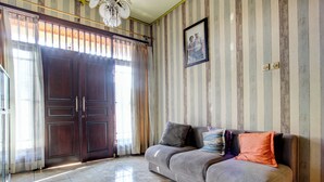 A living room with a grey sofa, striped wallpaper, a large wooden door, and a framed picture on the wall. - Hotel O Griya Pius Syariah Malioboro (Yogyakarta)