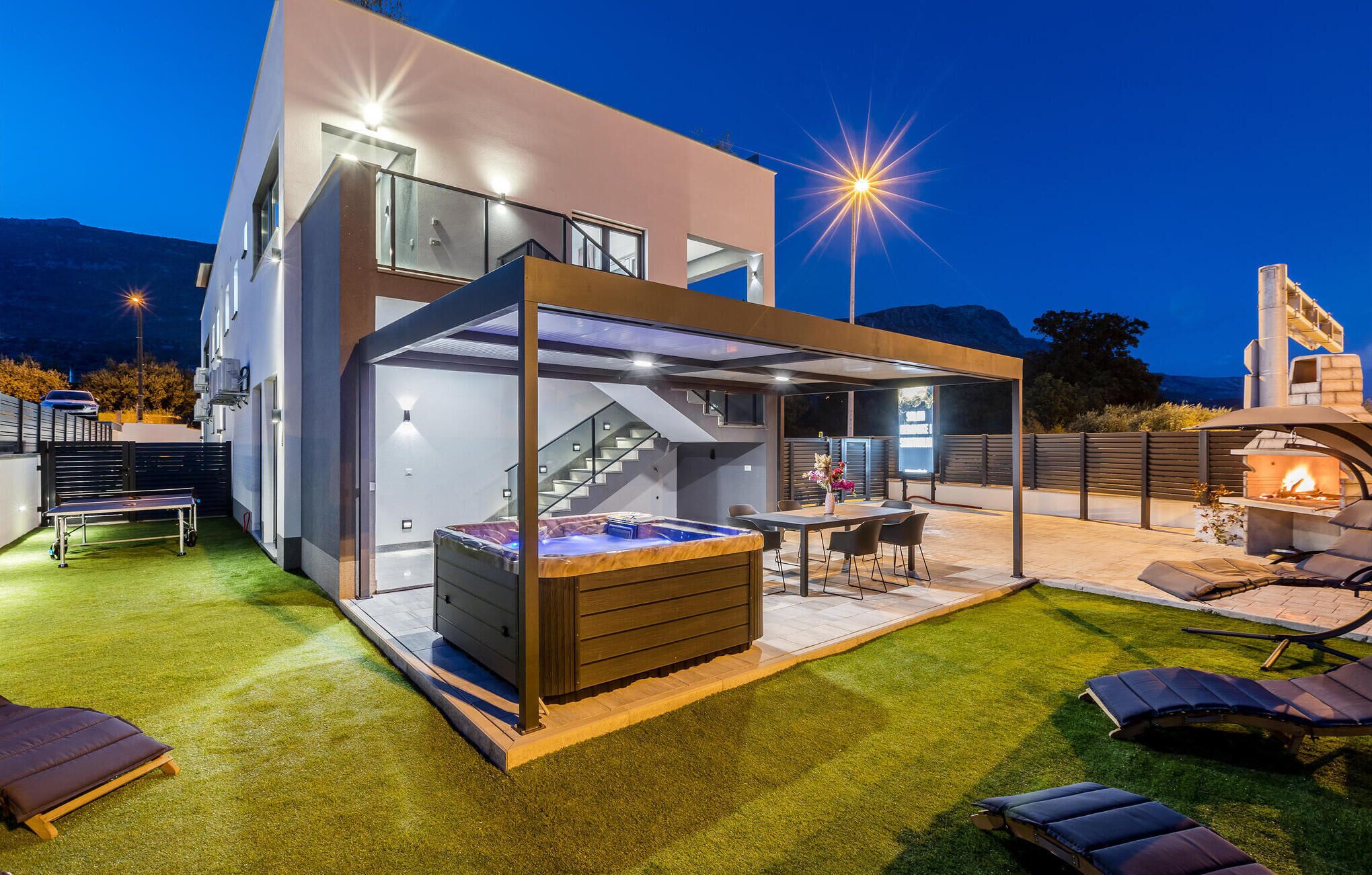 A modern outdoor patio area with a hot tub, seating, and a covered dining space.