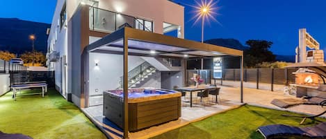 Een modern buitenterras met een jacuzzi, zitplaatsen en een overdekte eethoek.