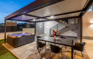 Une terrasse extérieure avec un jacuzzi, une table à manger et des chaises, ainsi qu’un escalier.