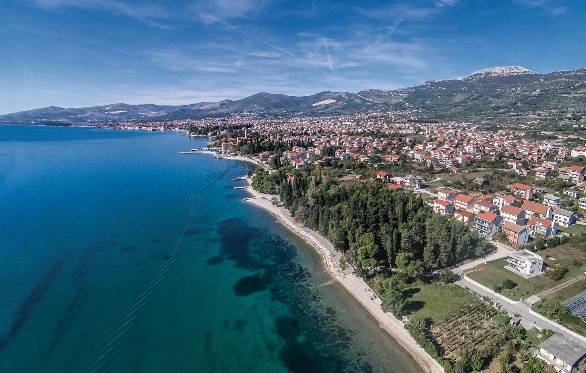 An aerial view of a coastal town with a long beachfront, dense residential area, and mountainous background.