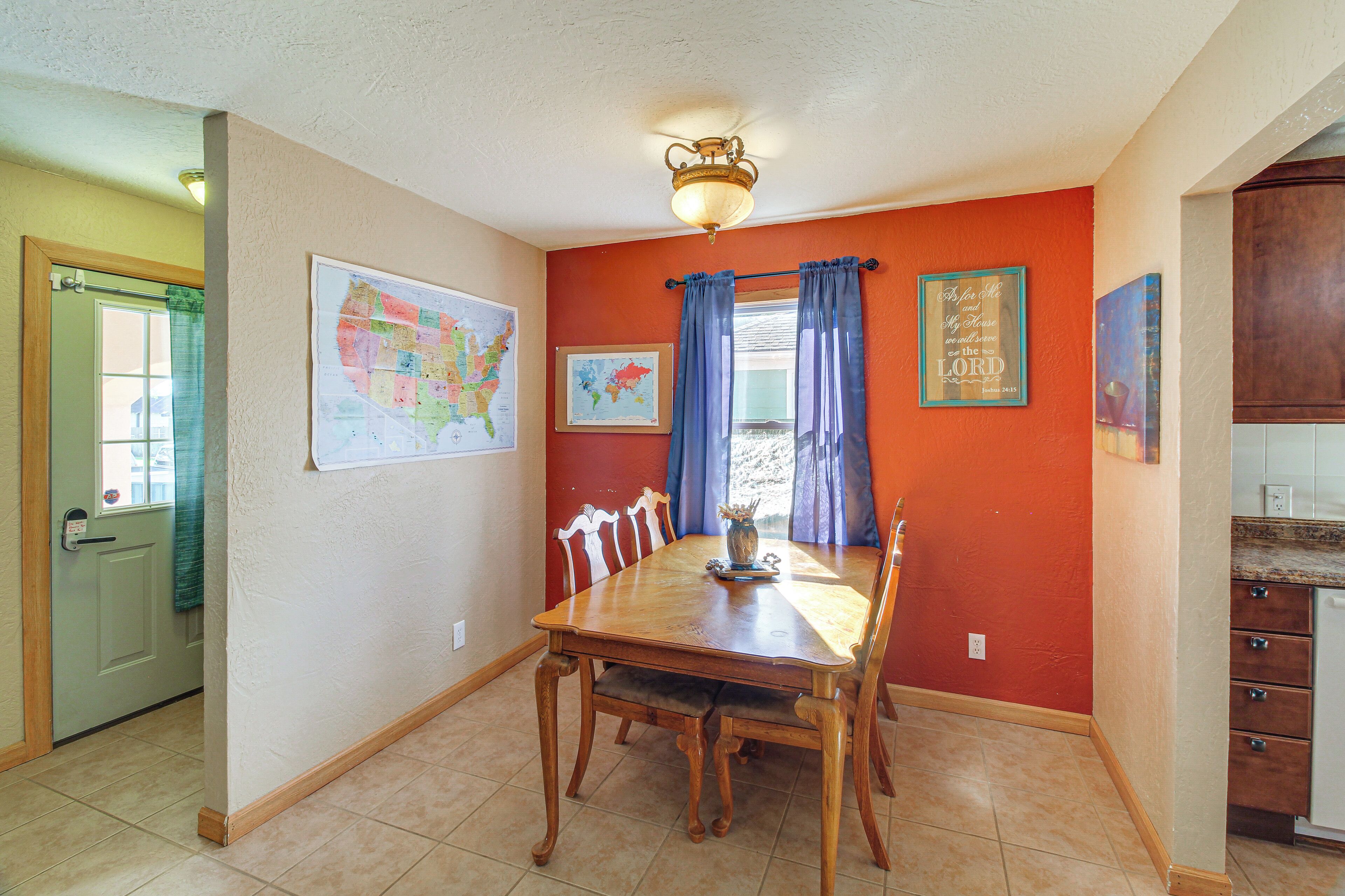 Une salle à manger avec une table et des chaises en bois, une carte accrochée au mur et un coin cuisine avec des placards.