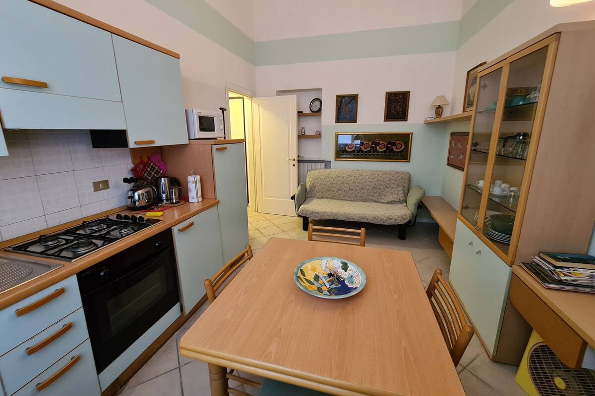 A compact kitchen with a dining area, a sofa, and a cabinet with glass doors.