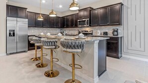 A modern kitchen with dark cabinets, stainless steel appliances, a marble island, and gold bar stools.