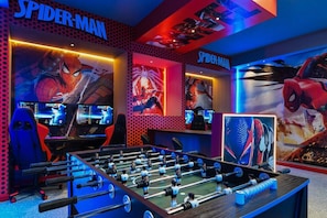 Et spillelokale med flere skærme, et bordfodboldbord og Spider-Man dekorationer.