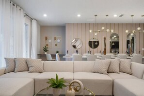En moderne stue med sofa, spiseområde og køkken i baggrunden.