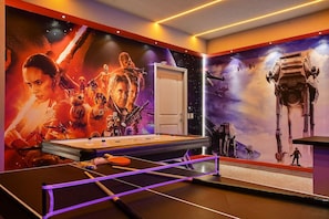 Une pièce avec une table de ping-pong, une porte et des œuvres d’art murales sur le thème de l’espace.
